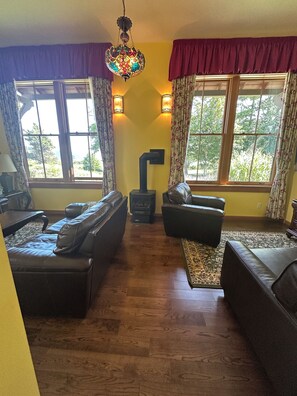 A living room with leather sofas, a fireplace, and large windows with curtains. - Captain's Suite - 2 Bedroom Condo in Eastsound across from the park (Eastsound)