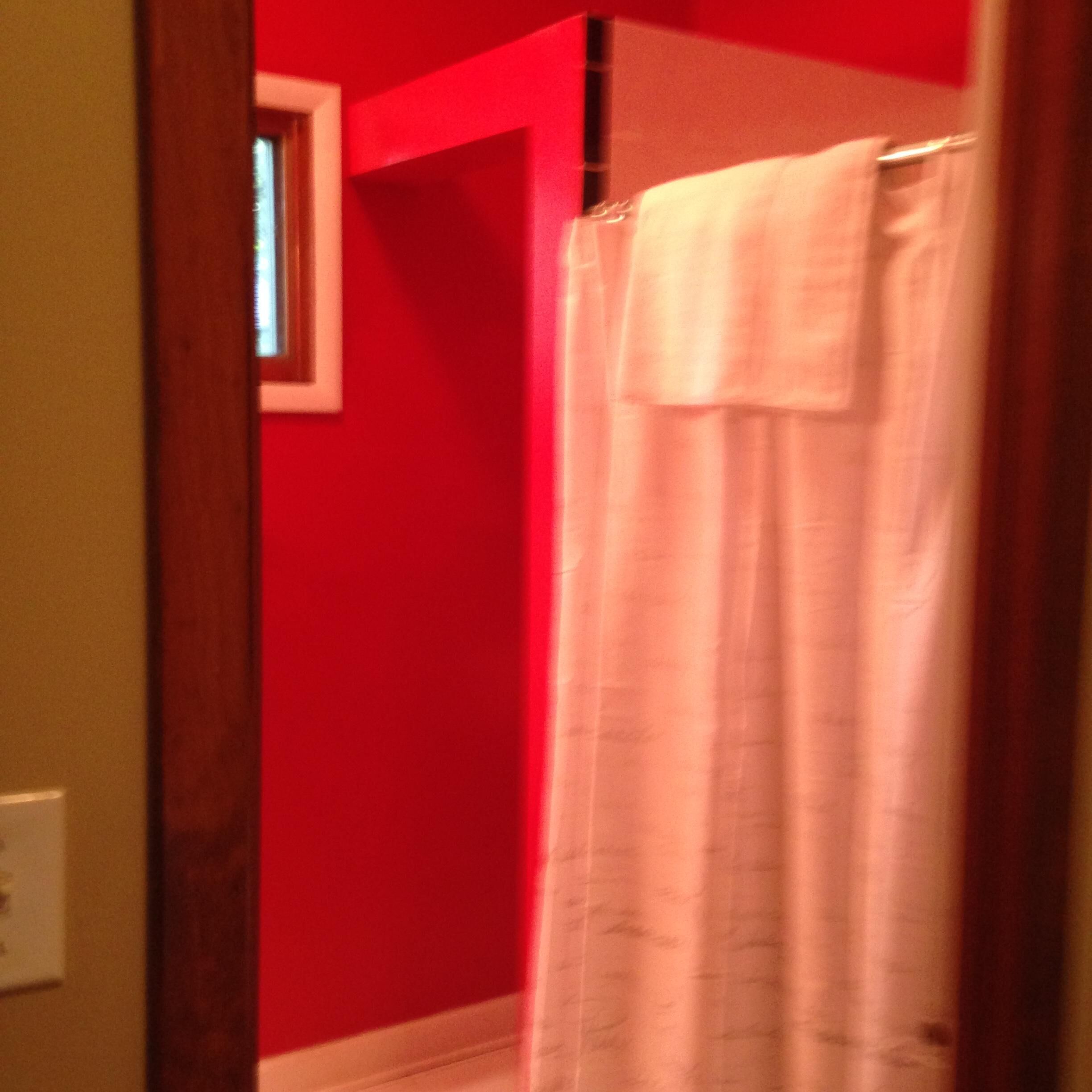 Un baño con paredes rojas y una cortina de ducha blanca.