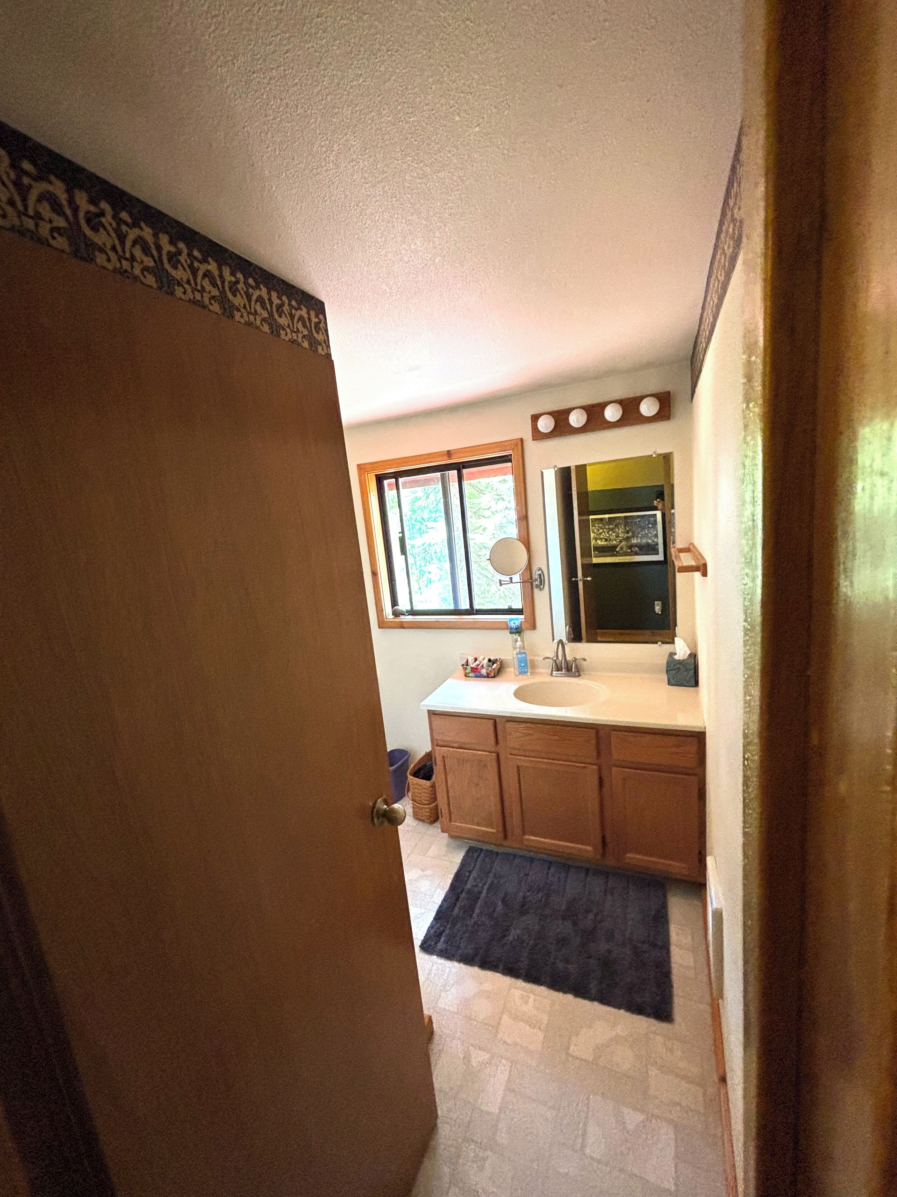 A bathroom with a wooden vanity, a sink, a mirror, and a window.