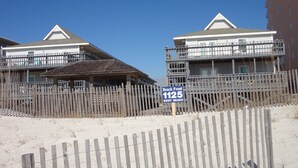 Una propiedad frente a la playa con cerca de madera, un letrero que indica 'Beach Front 1125 West Beach' y un edificio con balcón.