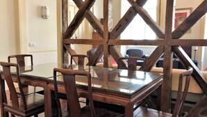 Ein Essbereich mit Glastisch, umgeben von Holzstühlen, einer Holzquerstrebenkonstruktion und Blick auf einen Raum mit Sofa und Fernseher.