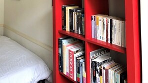 Ein Schlafzimmer mit einem Bett, einem roten Bücherregal und drei gerahmten Postern an der Wand.
