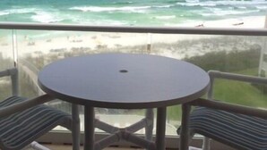 A balcony with a round table and two chairs, overlooking a beach and ocean. - Regency Towers 707 East Tower   Fall is Better at the Beach!  (Pensacola Beach)