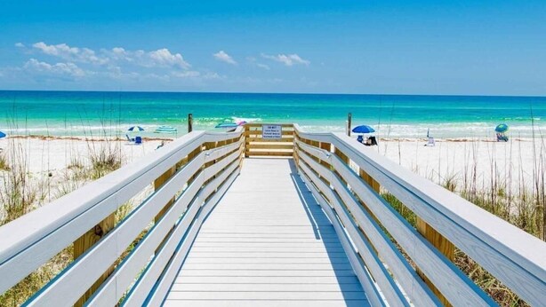 A wooden boardwalk leading to a beach with clear blue water and a few beach umbrellas. - Regency Towers 707 East Tower   Fall is Better at the Beach!  (Pensacola Beach)