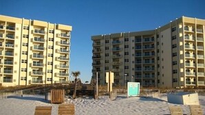 A beachfront hotel with multiple floors, outdoor seating, and a sandy beach area. - Regency Towers 707 East Tower   Fall is Better at the Beach!  (Pensacola Beach)