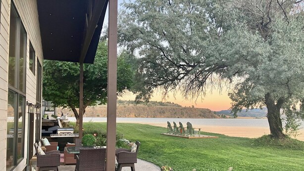 Une terrasse avec mobilier d’extérieur, un barbecue et une vue sur un lac et des collines.