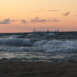 A beach with waves and a distant city skyline. - Restored Cottage Across The Street From The Beach! (Gary)