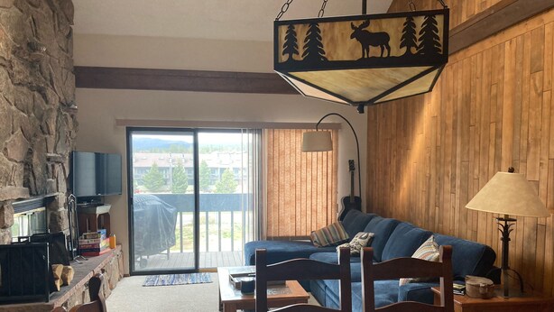 A cozy living room with a blue sofa, wooden dining table, and a stone wall. - Great family ski condo with access to all the Fraser valley has to offer (Fraser)