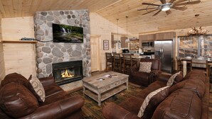 Un acogedor interior de cabaña con chimenea de piedra, sofás de cuero, comedor y cocina.