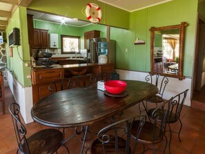 A dining area with a wooden table and metal chairs, a kitchen with green walls and wooden cabinets, and a life preserver hanging from the ceiling. - COUNTRY LAKE HOUSE (Panajachel)