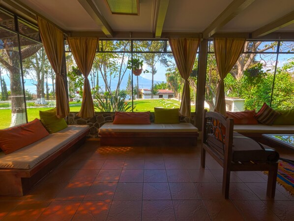 A room with a large window, a sofa, a chair, and a view of a garden and mountains. - COUNTRY LAKE HOUSE (Panajachel)
