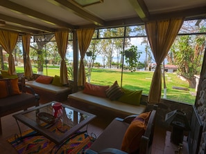 A spacious living area with a large window offering a view of a well-maintained lawn and distant buildings. - COUNTRY LAKE HOUSE (Panajachel)