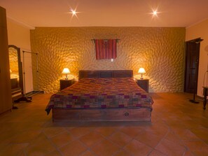 A bedroom with a large bed, two bedside lamps, a stone wall, and a window with a curtain. - COUNTRY LAKE HOUSE (Panajachel)