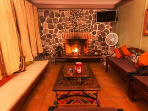 A cozy living room with a stone wall, a fireplace, a sofa, a coffee table, and a fan. - COUNTRY LAKE HOUSE (Panajachel)