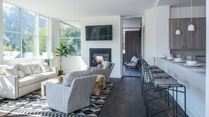 Ein modernes Wohnzimmer mit einer Couch, Sesseln, einem Kamin und einer Küchenzeile mit Barhocker.