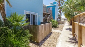 A blue building with a wooden deck, palm trees, and a concrete pathway.
