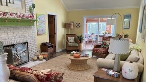A cozy living room with a fireplace, wicker furniture, a coffee table with pumpkins, and a view of the outdoors. - Key West in Cape May: Hot tub open year round! Dog friendly! (Villas)