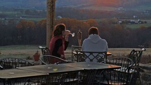 Zwei Personen sitzen an einem Tisch mit Blick auf einen Sonnenuntergang über einer hügeligen Landschaft.