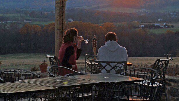 Two people seated at a table with a view of a sunset over a hilly landscape.