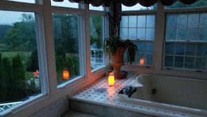 A bathroom with a bathtub, a window with a view of greenery, and a candle on the windowsill.