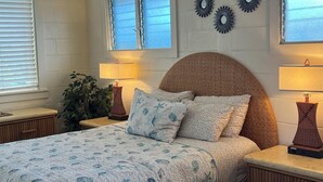Un dormitorio con cama, dos mesitas de noche, una ventana con persianas y decoración en la pared.