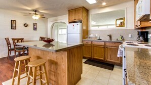Una cocina con armarios de madera, un refrigerador blanco, encimera de granito y un ventilador de techo.