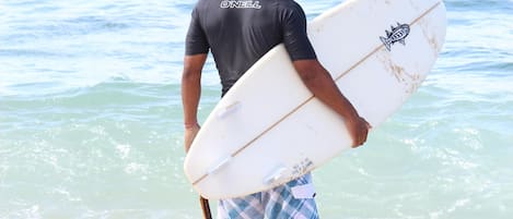 A man carrying a surfboard, wearing a dark wetsuit and blue shorts, walking towards the ocean.