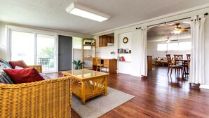 Un salón espacioso con una mesa de comedor de madera, un sofá de mimbre y un amplio ventanal que proporciona luz natural.