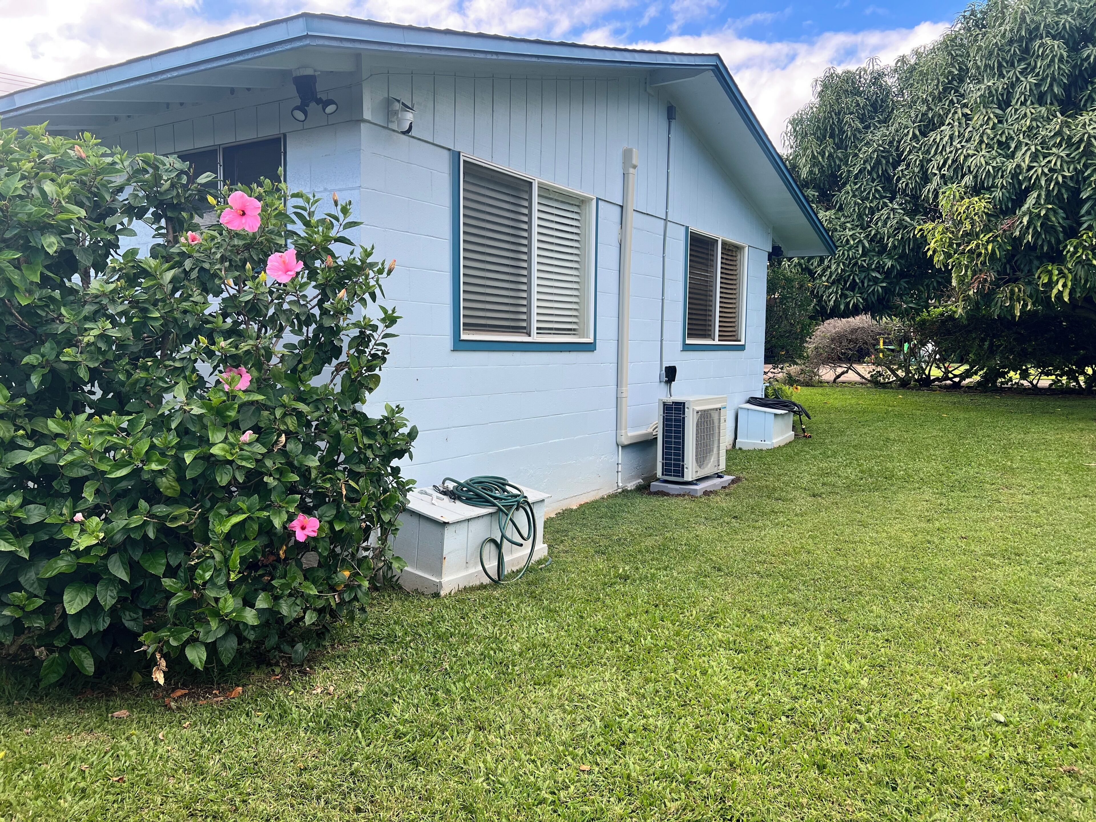 A light blue house with a small porch, a lawn, and a bush with pink flowers.