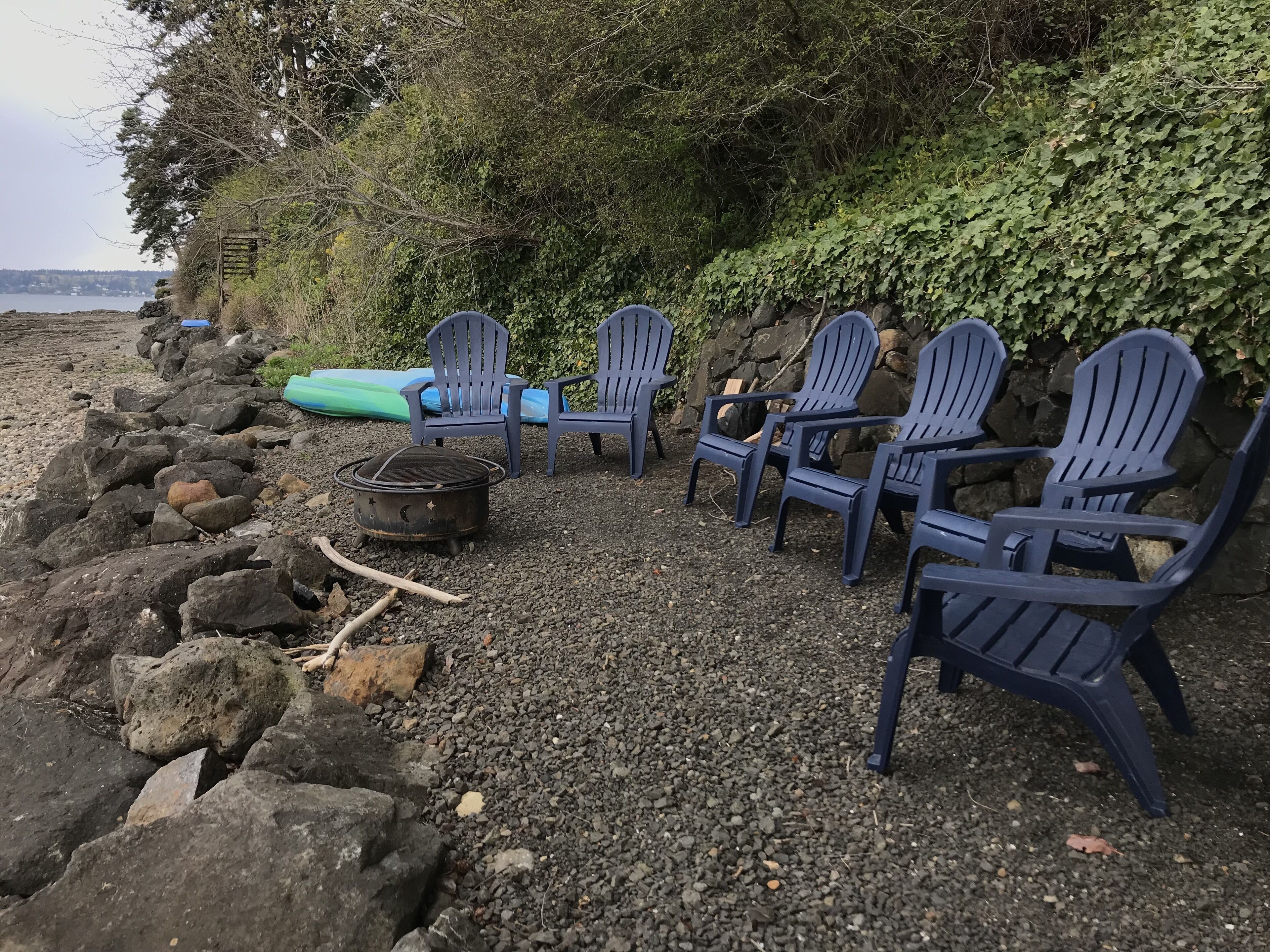 Eine Reihe Adirondack-Stühle an einem felsigen Strand mit Blick auf den Ozean.