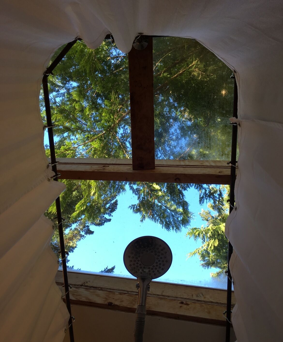 A room with a large window, a wooden beam, and a showerhead.