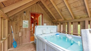 A wooden cabin with a hot tub, a door leading to a room, and a mop leaning against the wall. - Blue Rose Cabins - Country Cottage (Logan)