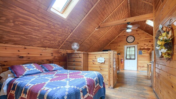 A cozy wooden room with a bed, a dresser, a fan, and a door with a sign. - Blue Rose Cabins - Country Cottage (Logan)