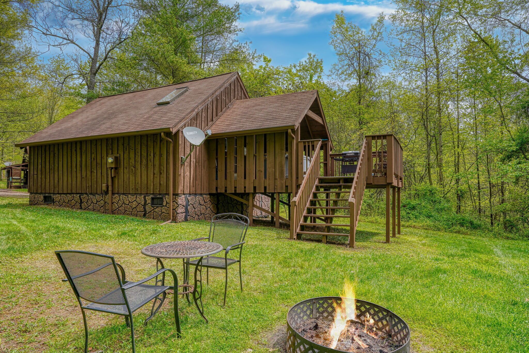 A rustic wooden cabin with a stone foundation, a fire pit, and outdoor seating.