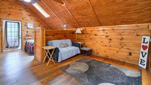 A cozy cabin room with a bed, a small table, a chair, a fan, and a sign that says 'LOVE'. - Blue Rose Cabins - Country Cottage (Logan)