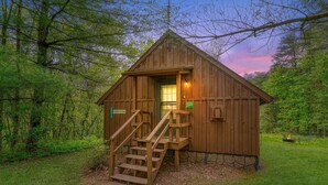 A wooden cabin with a staircase leading to the entrance, surrounded by lush greenery. - Blue Rose Cabins - Country Cottage (Logan)