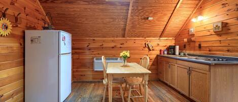 Une cuisine compacte aux murs en bois, avec un réfrigérateur blanc, une table à manger et des chaises, et une lucarne au-dessus.