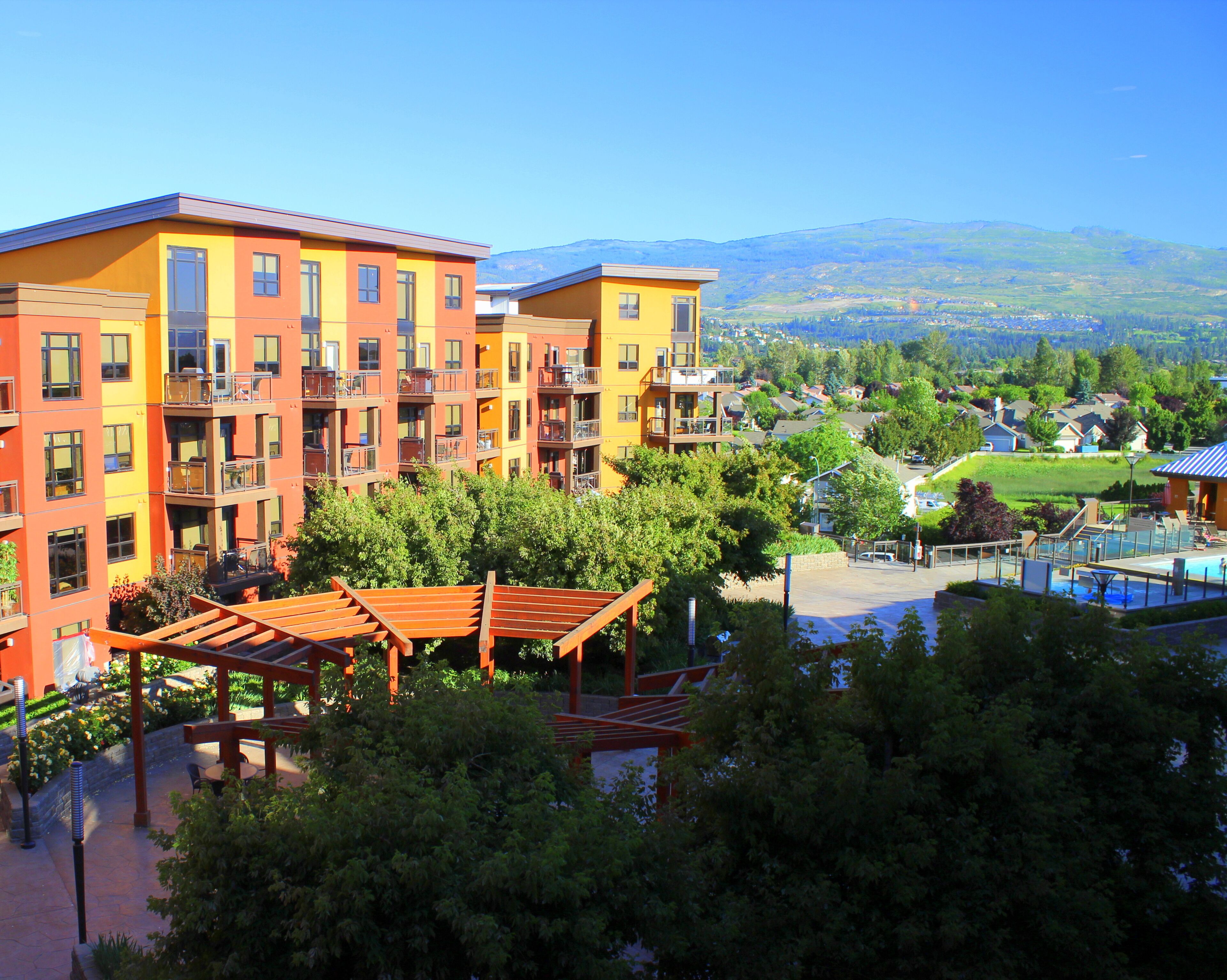A multi-story hotel with balconies, a swimming pool, and a view of a mountainous landscape.