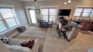 A spacious living area with a sofa, a coffee table, and a dining table with chairs. There is a kitchen area with a countertop and cabinets.
