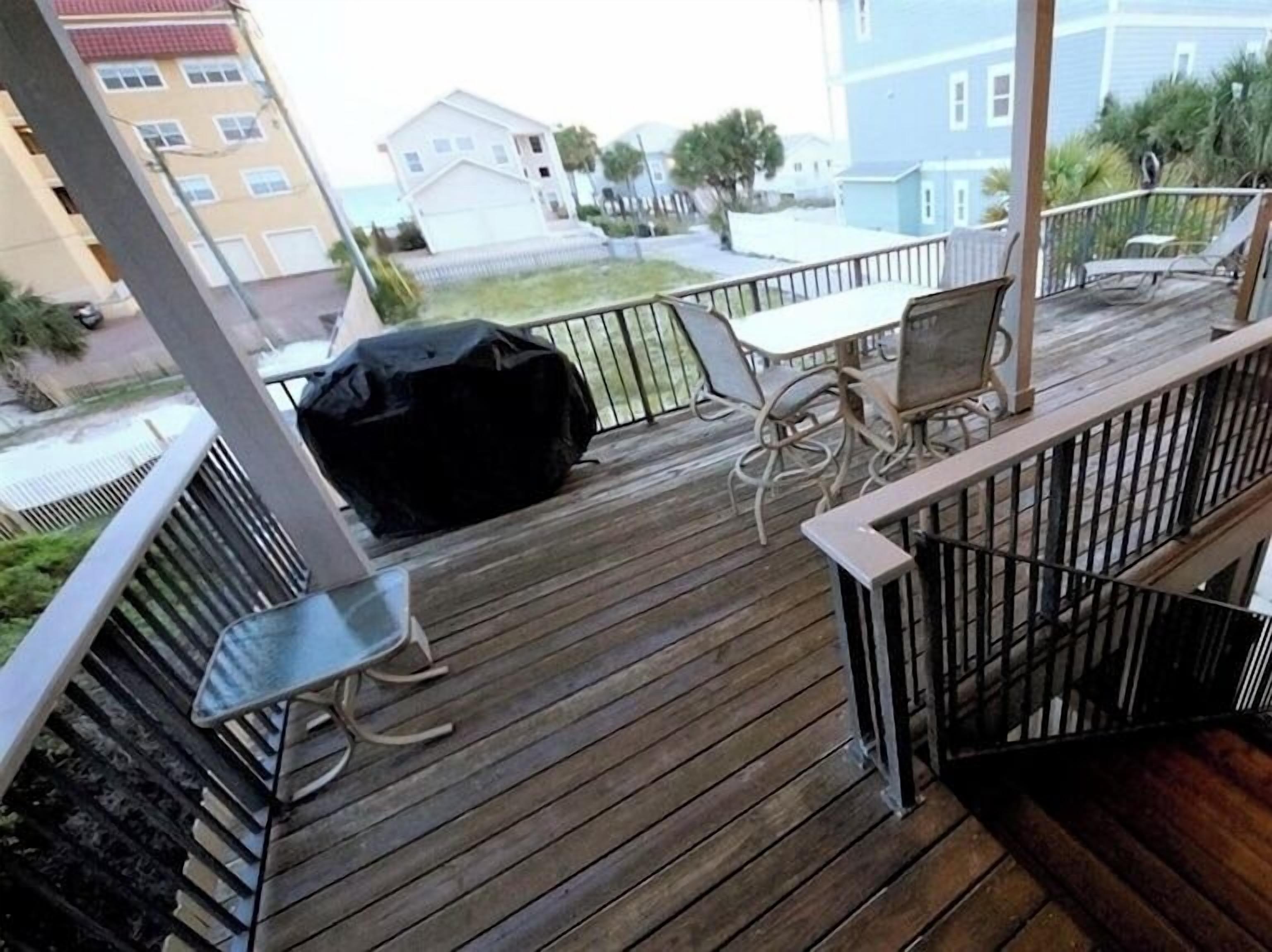 Eine Holzterrasse mit Gartenmöbeln, einem überdachten Grill und Blick auf benachbarte Gebäude.