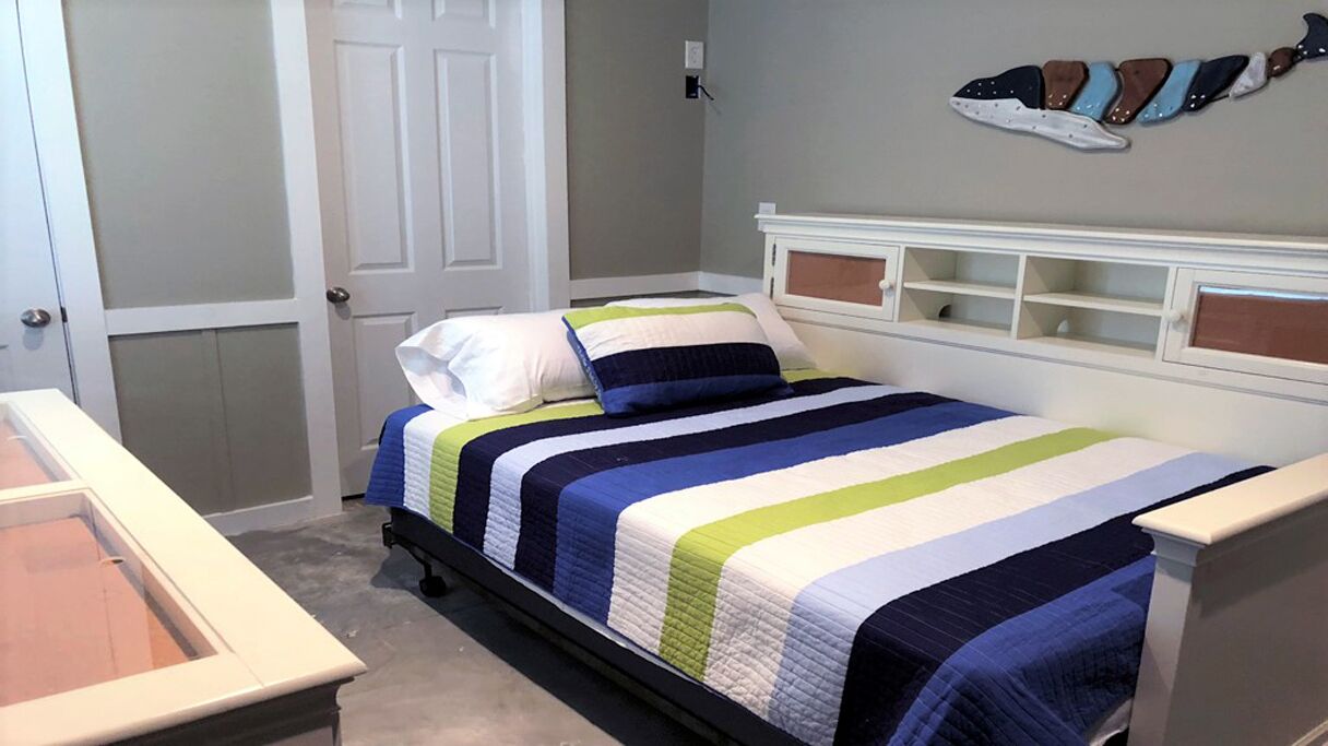 A bedroom with a bed, a nightstand, a door, and a wall-mounted shelf.