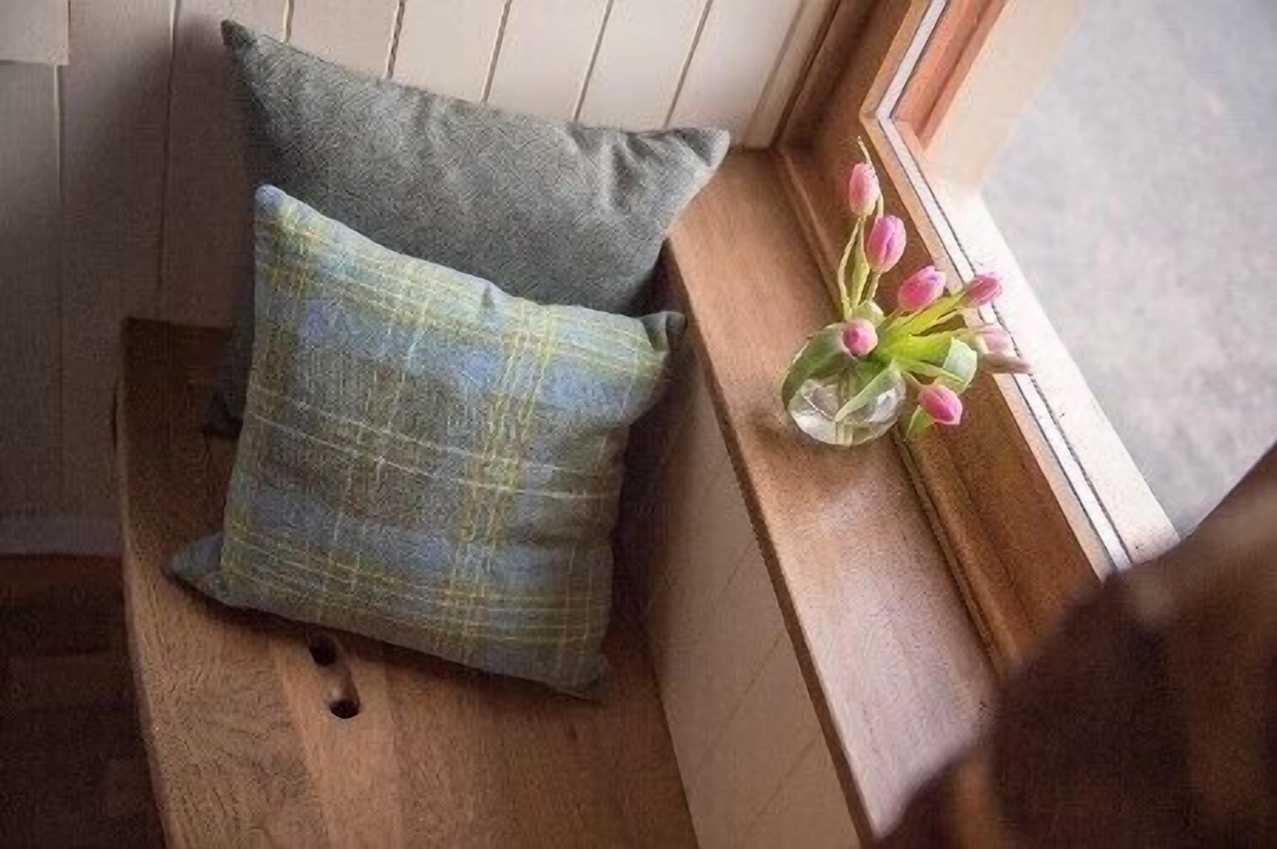 A window sill with a cushion and a vase of flowers.