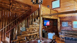 A log cabin interior with a wooden staircase, a dining area with a table and chairs, a television, and a sofa. - Dogwood Cabin, Deer Lodge Cabin Rentals is a Secluded Ozark Mountain Log Cabin.  (Jasper)