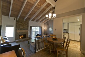 A spacious living area with a stone fireplace, wooden ceiling beams, a dining table with chairs, and a kitchen area with cabinets and a refrigerator. - Remodeled Snowcreek Condo - 2 Bdrms /2 Bthrms /and small loft (Sun Valley)