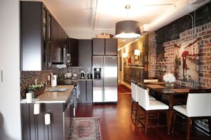 A modern kitchen with dark cabinets, stainless steel appliances, and a dining area with a brick wall and a mural. - Fabulous location, wonderful accommodations, walk to everything!! (Savannah)