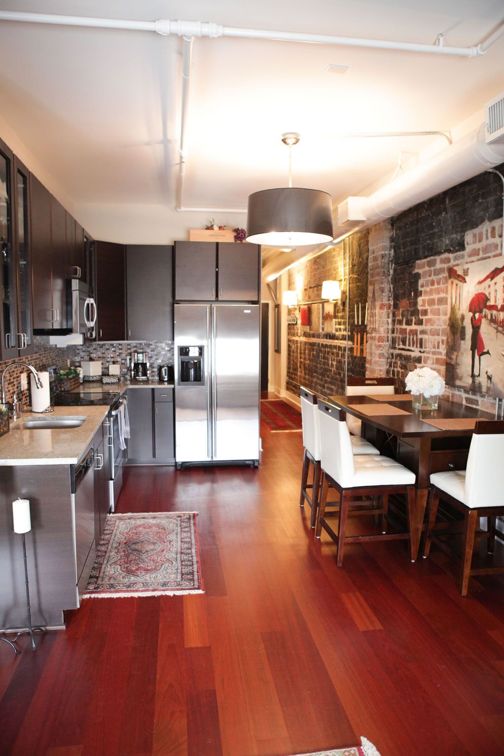 Una cocina moderna con electrodomésticos de acero inoxidable, una zona de comedor con un mural de pared de ladrillo y suelo de madera.