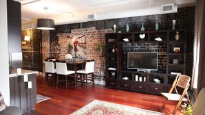 Een moderne woonkamer met een bakstenen muur, houten meubels, een flatscreen televisie en decoratieve objecten.