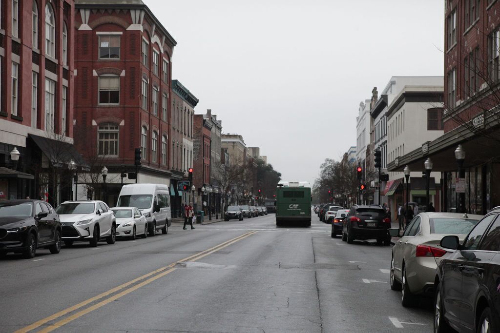 A street lined with buildings, cars parked along the sides, and a green bus in the center.