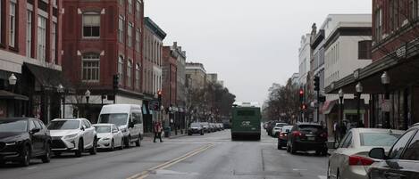 A street lined with buildings, cars parked along the sides, and a green bus in the center.