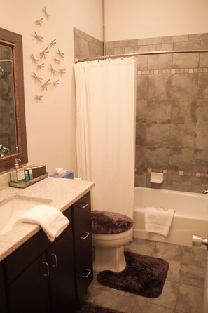 A bathroom with a toilet, a bathtub, a shower curtain, a sink with toiletries, and a mirror. - Fabulous location, wonderful accommodations, walk to everything!! (Savannah)